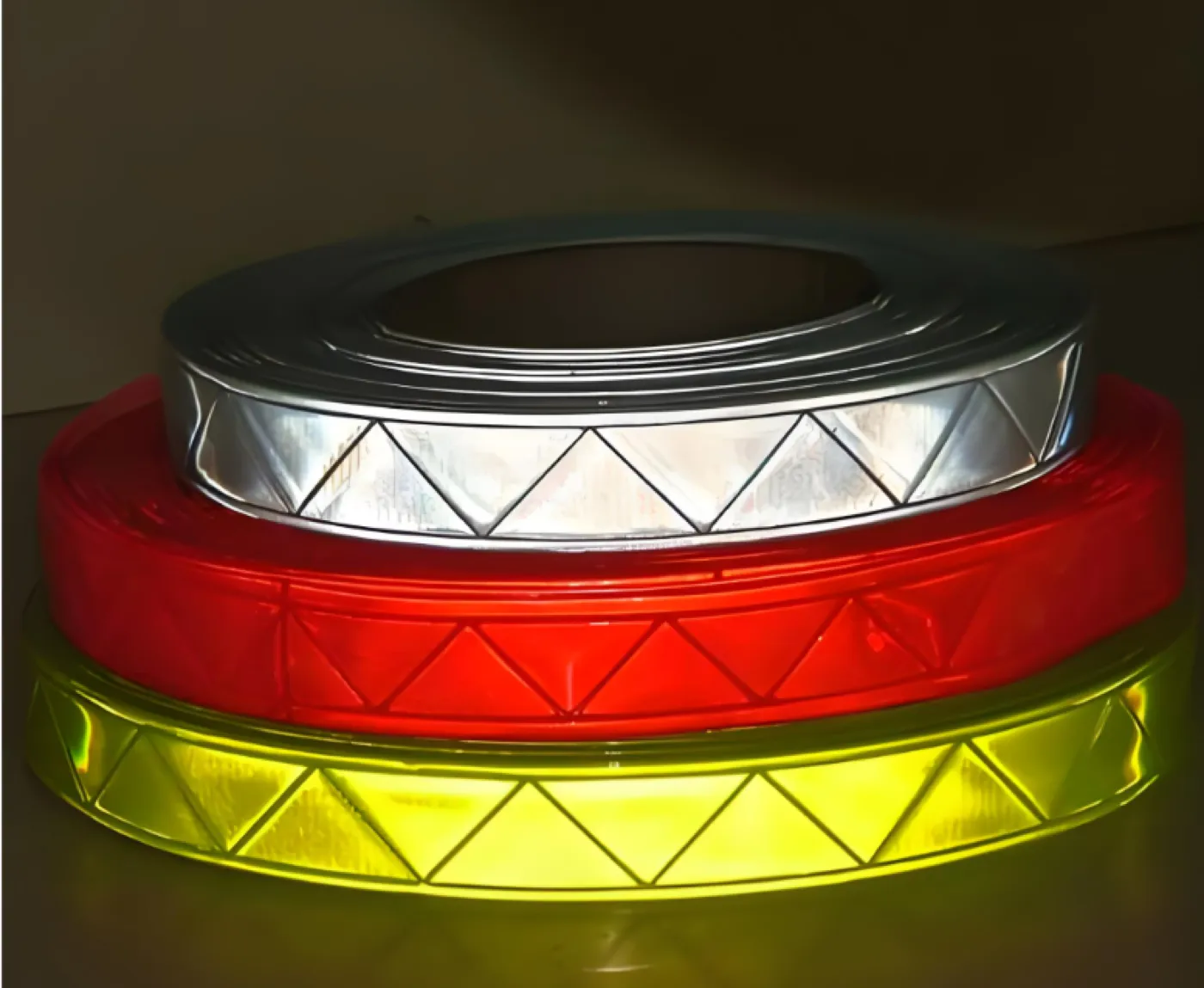 Prismatic reflective tape in silver, red and yellow, three rolls stacked showing the microprismatic structure